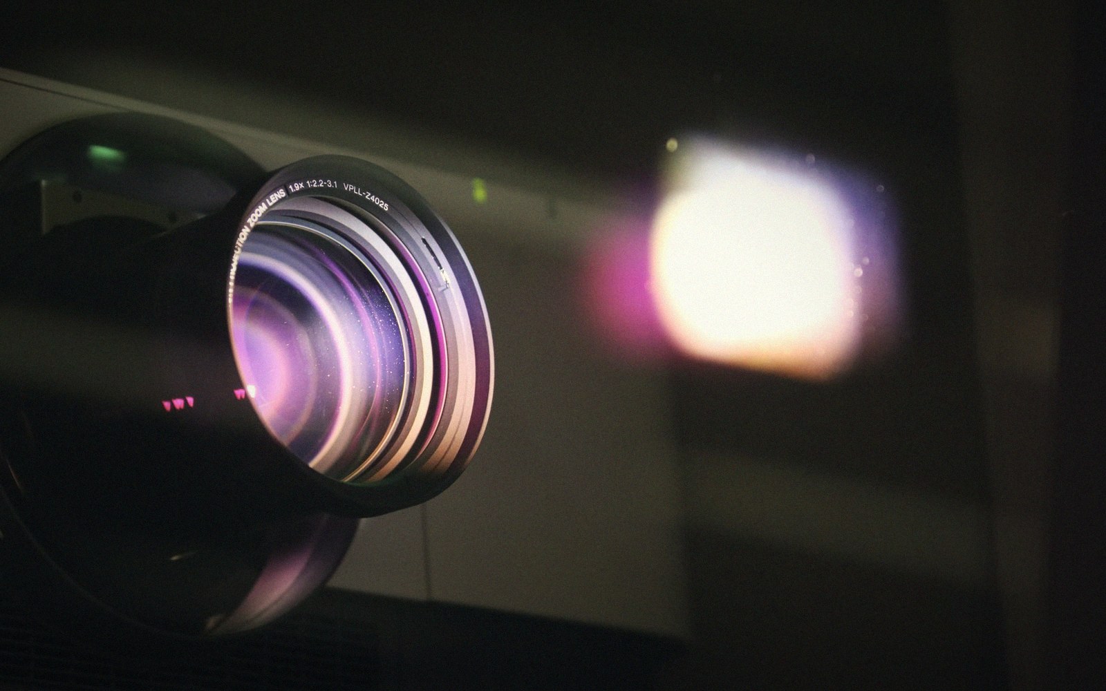 The rectangular aperture of a 35mm projection booth seen from inside, the beam of light cutting through haze toward an unseen screen